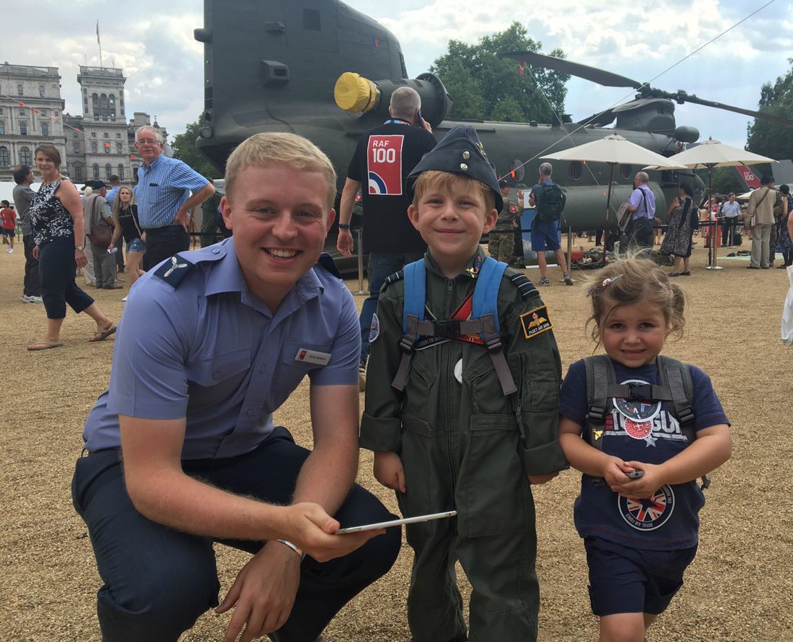 An RAF man crouches smiling for a photo with two small children, one in an army uniform