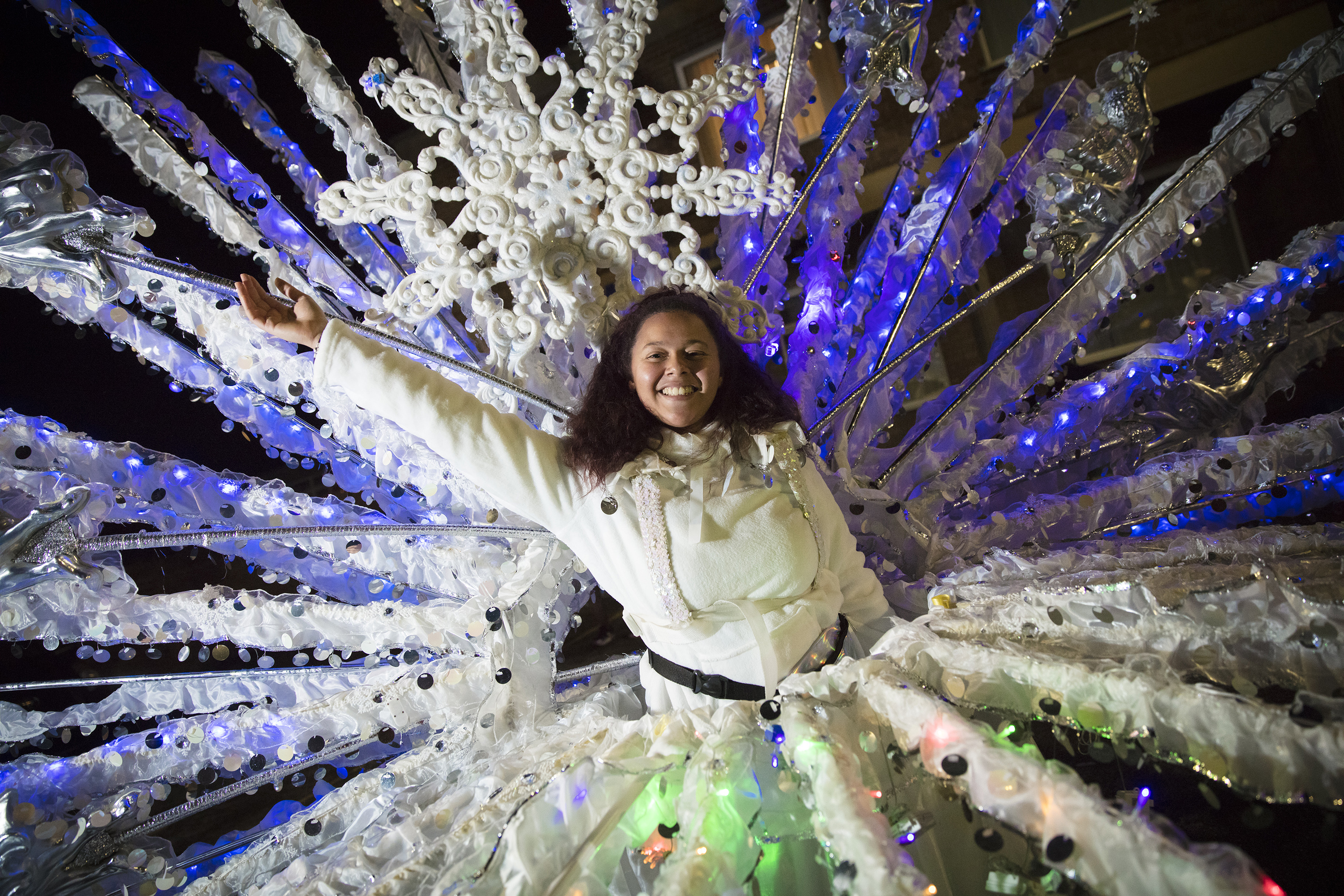 A young woman wears a fantastical white costume of feathers and sparkles and snowflakes